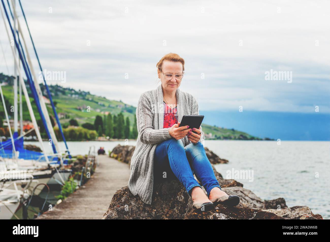 Donna di mezza età che riposa vicino al lago, che usa un tablet pc all'aperto Foto Stock