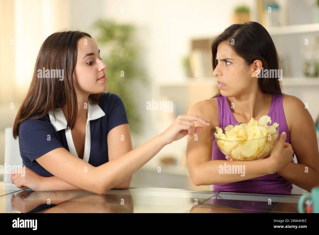 Donna egoista che protegge le sue patatine fritte da un amico a casa Foto Stock