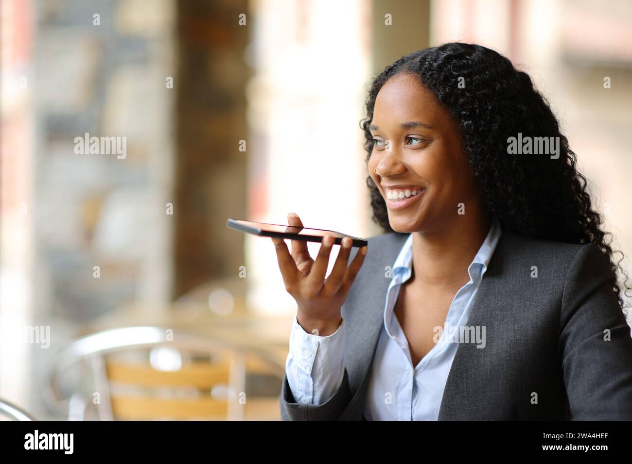 Felice dirigente nero che dettava un messaggio al telefono in un bar Foto Stock