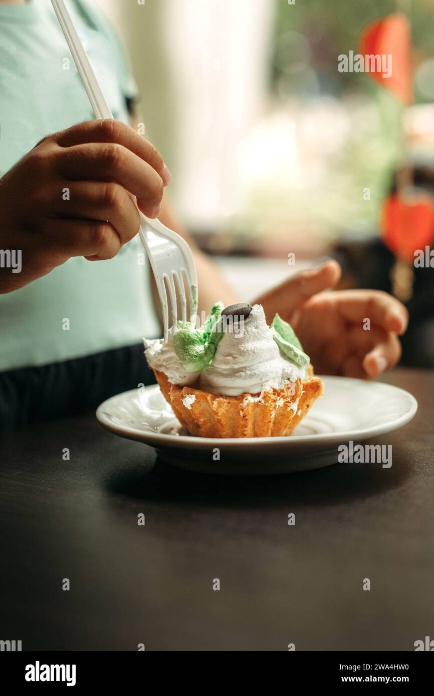 Un bambino mangia una torta con soffice crema proteica con una forchetta. Primo piano, telaio verticale. Foto Stock