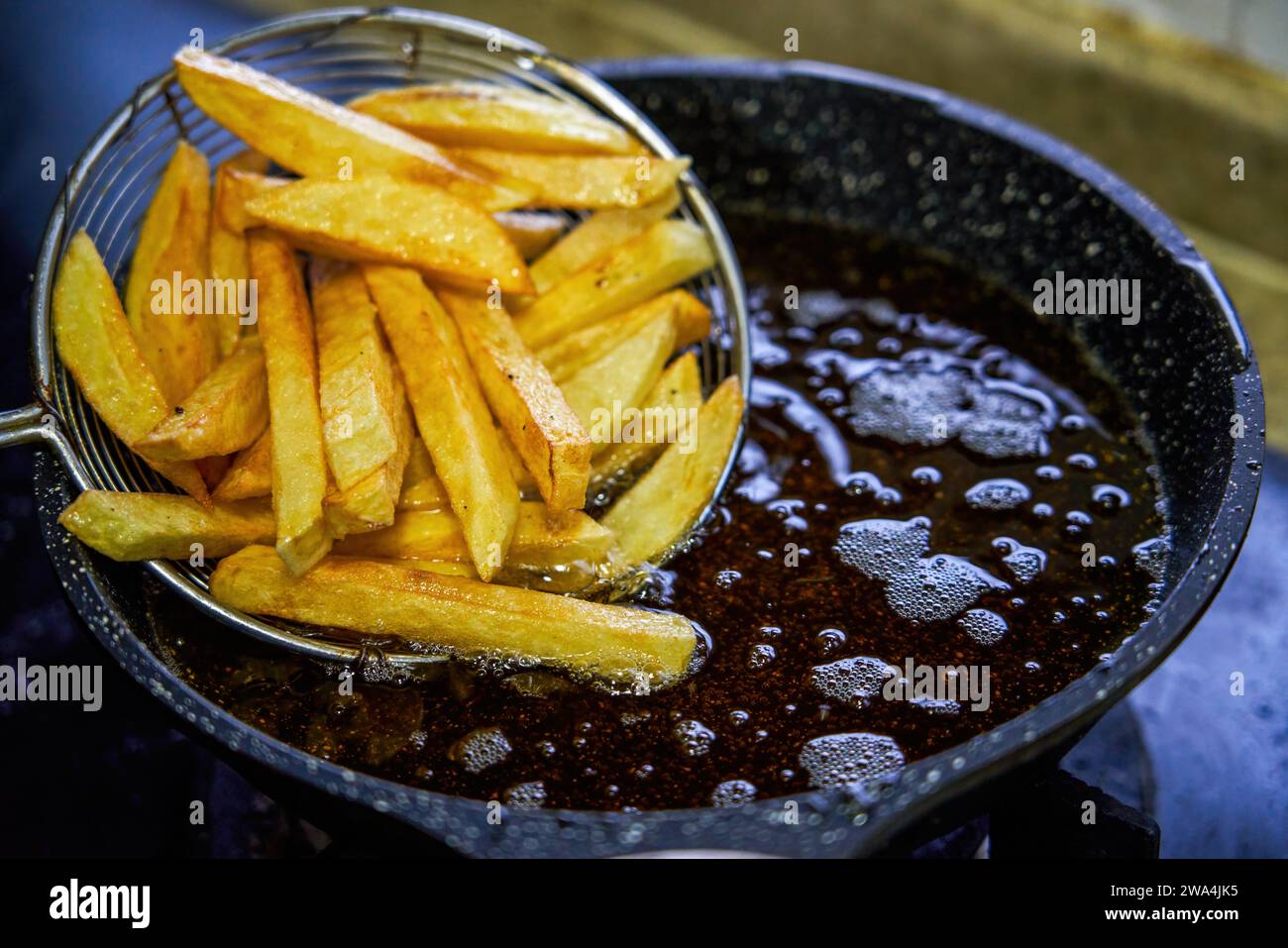 Uno chef che frigge patatine fritte in una padella Foto Stock