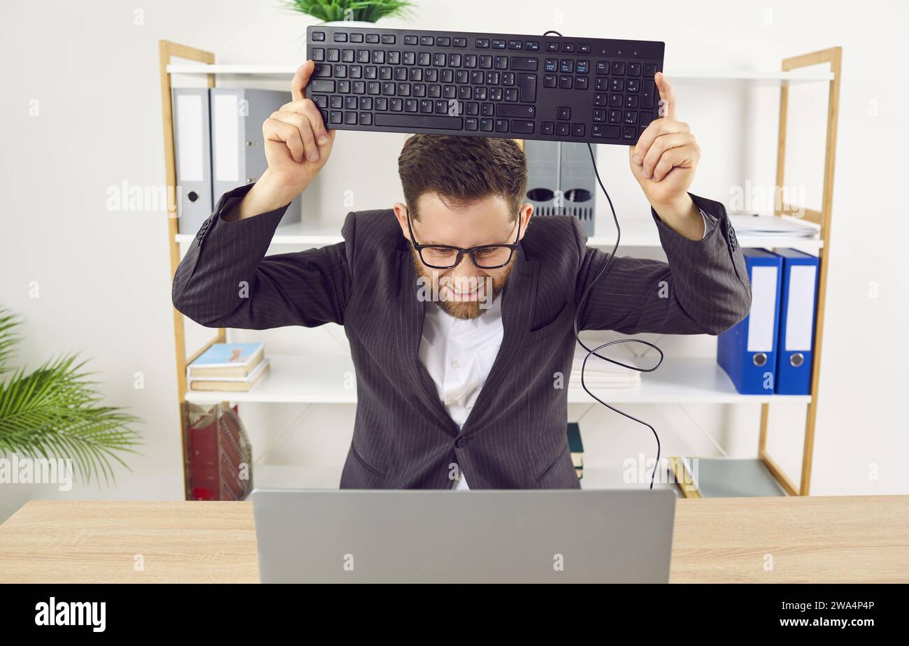 Il lavoratore in ufficio si arrabbia a causa di un problema del computer e vuole rompere la tastiera Foto Stock