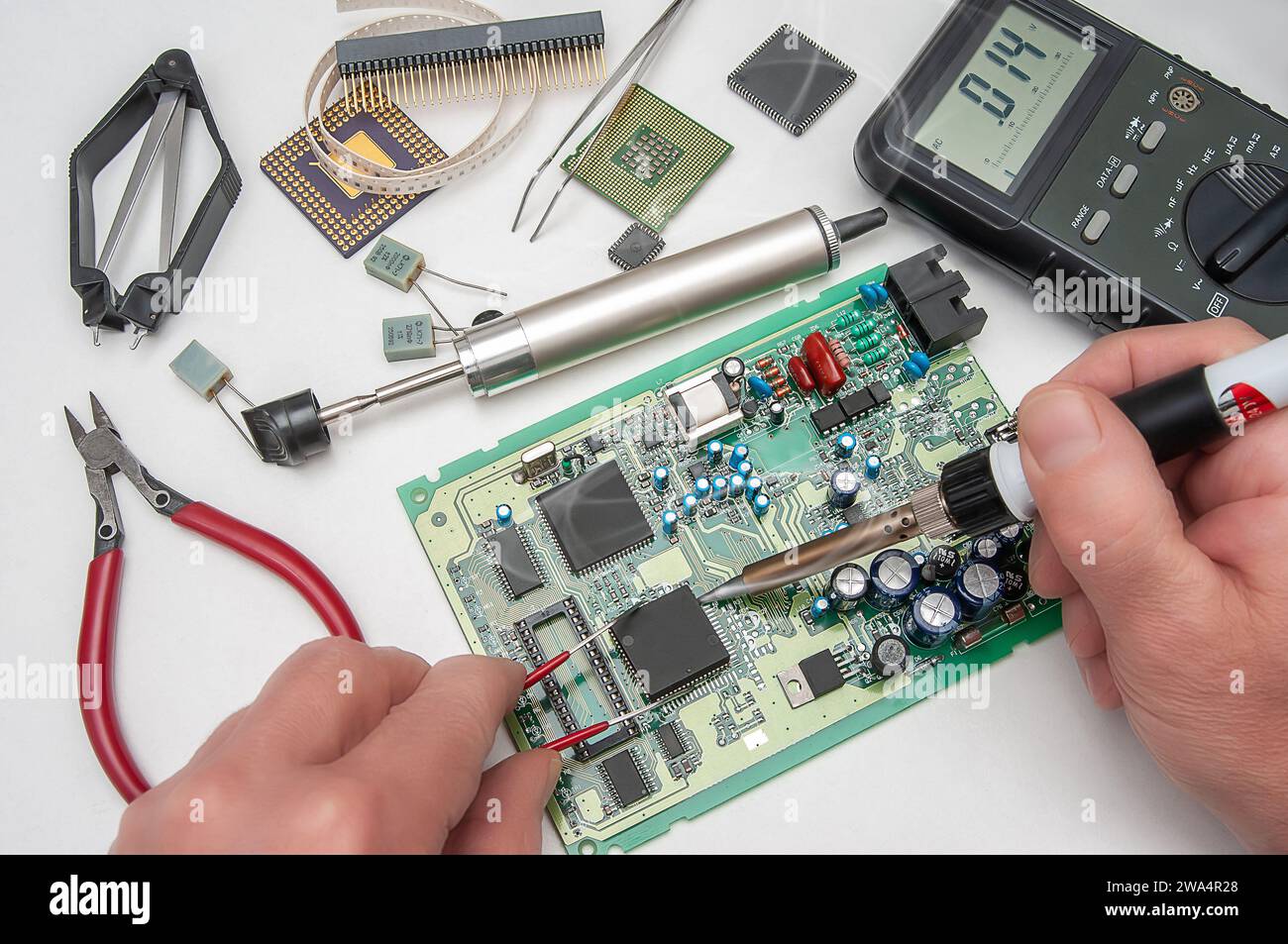 Primo piano delle mani di un tecnico in un'officina. Il riparatore sta saldando un IC in un contenitore PLCC sulla scheda a circuito stampato di un dispositivo elettronico. Foto Stock