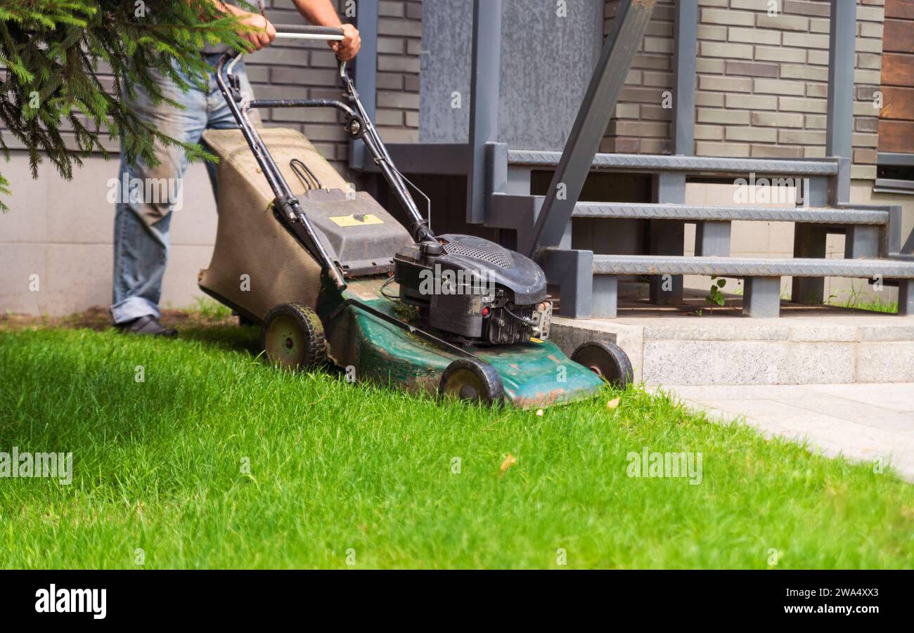 Il giardiniere taglia il prato verde nel cortile. Giardinaggio e cura del prato. Foto Stock