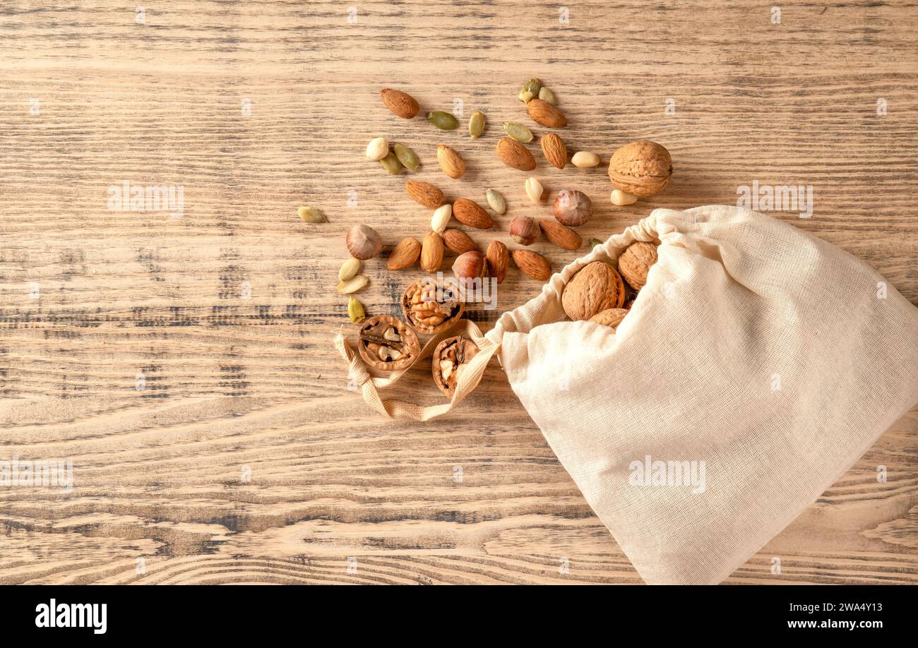Noci di mandorle, nocciole, noci e semi dolci in un sacchetto di burlap su uno sfondo di legno. Vista dall'alto. Foto Stock