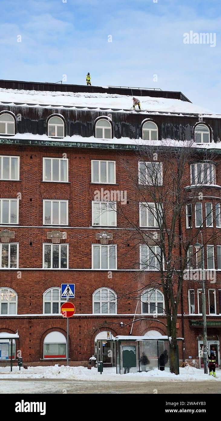 Un team di lavoratori che pulisce la neve dal tetto di un edificio residenziale a più piani dopo la nevicata. Helsinki, Finlandia. 2023. Foto del telefono. Foto Stock