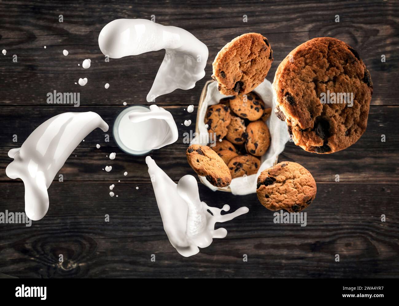 Bicchiere di latte con gustosi biscotti in un cestino. Vista dall'alto. Spruzzi di latte e biscotti volanti. Sfondo sfocato del vecchio tavolo in legno. Rustico e polveroso Foto Stock