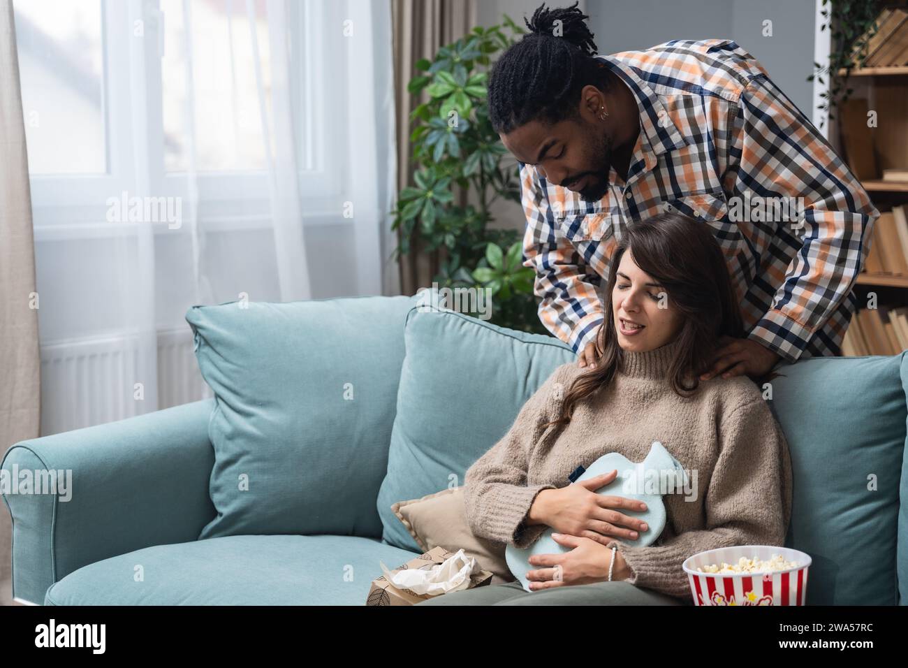 Coppia di razza mista uomo afro-americano e donna bianca, maschio massaggia la sua fidanzata o moglie durante il periodo mestruale mentre si siede a casa. Amore, suppo Foto Stock