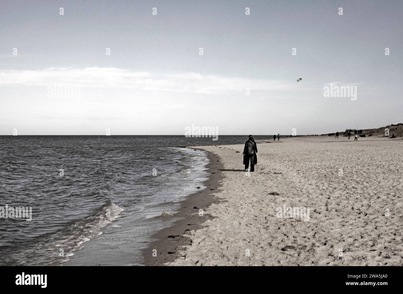 Fotografia monocromatica della costa sabbiosa del Mare del Nord con una donna sola con un aquilone nero in una riserva naturale vicino a Cuhhaven, Brema, GE Foto Stock