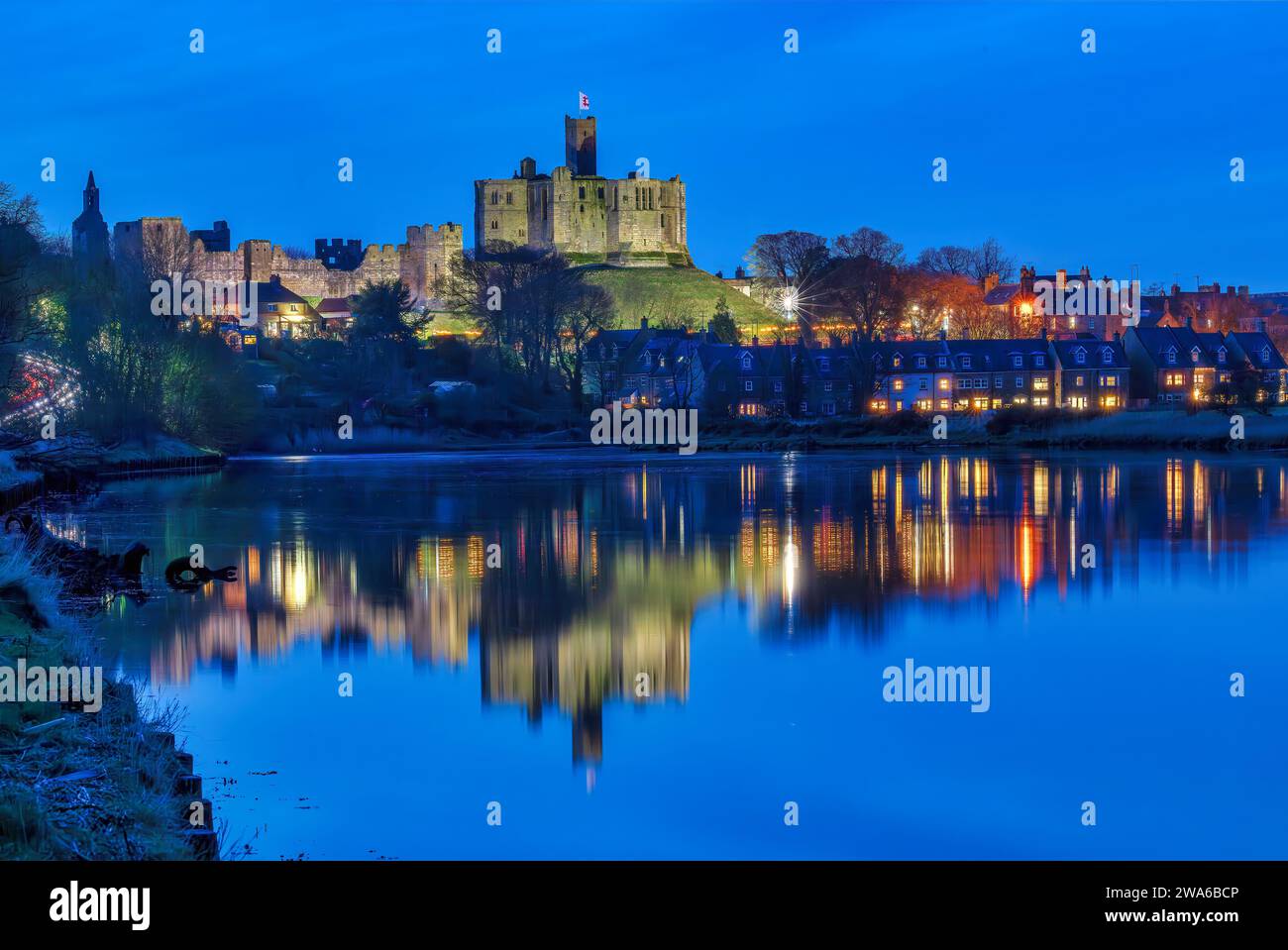 Ammira al crepuscolo il castello di Warkworth e il villaggio di Warkworth riflesso nel fiume Coquet, visto dall'amble con il castello di Warkworth illuminato. Foto Stock