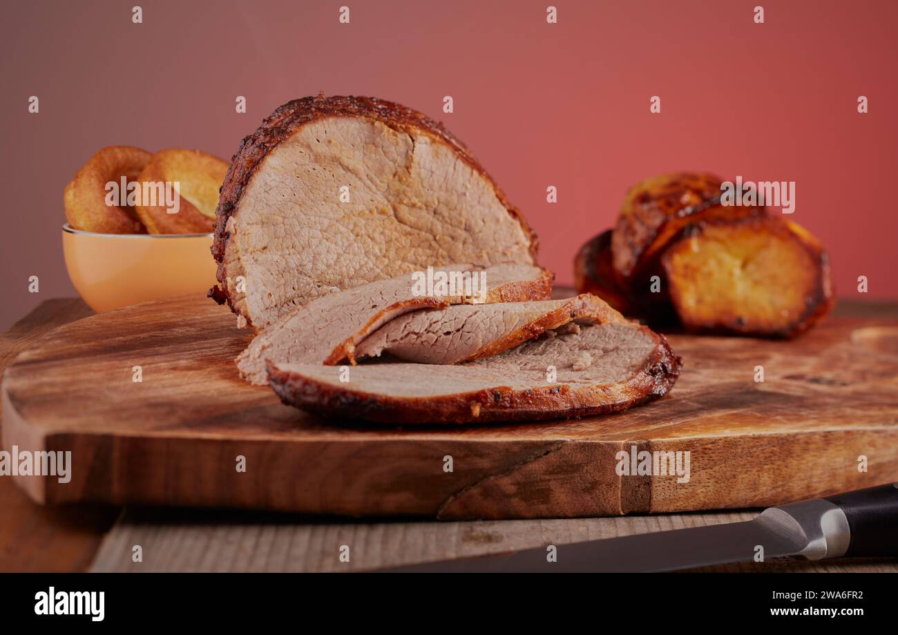 Arrosto di manzo tagliato a fette con budini dello Yorkshire e patate arrosto sullo sfondo. Foto Stock