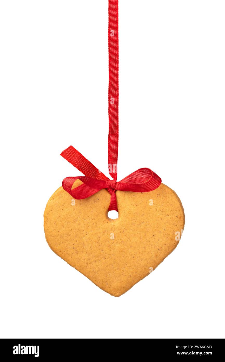 Un unico biscotto dolce a forma di cuore appeso a un nastro rosso su sfondo bianco da vicino Foto Stock