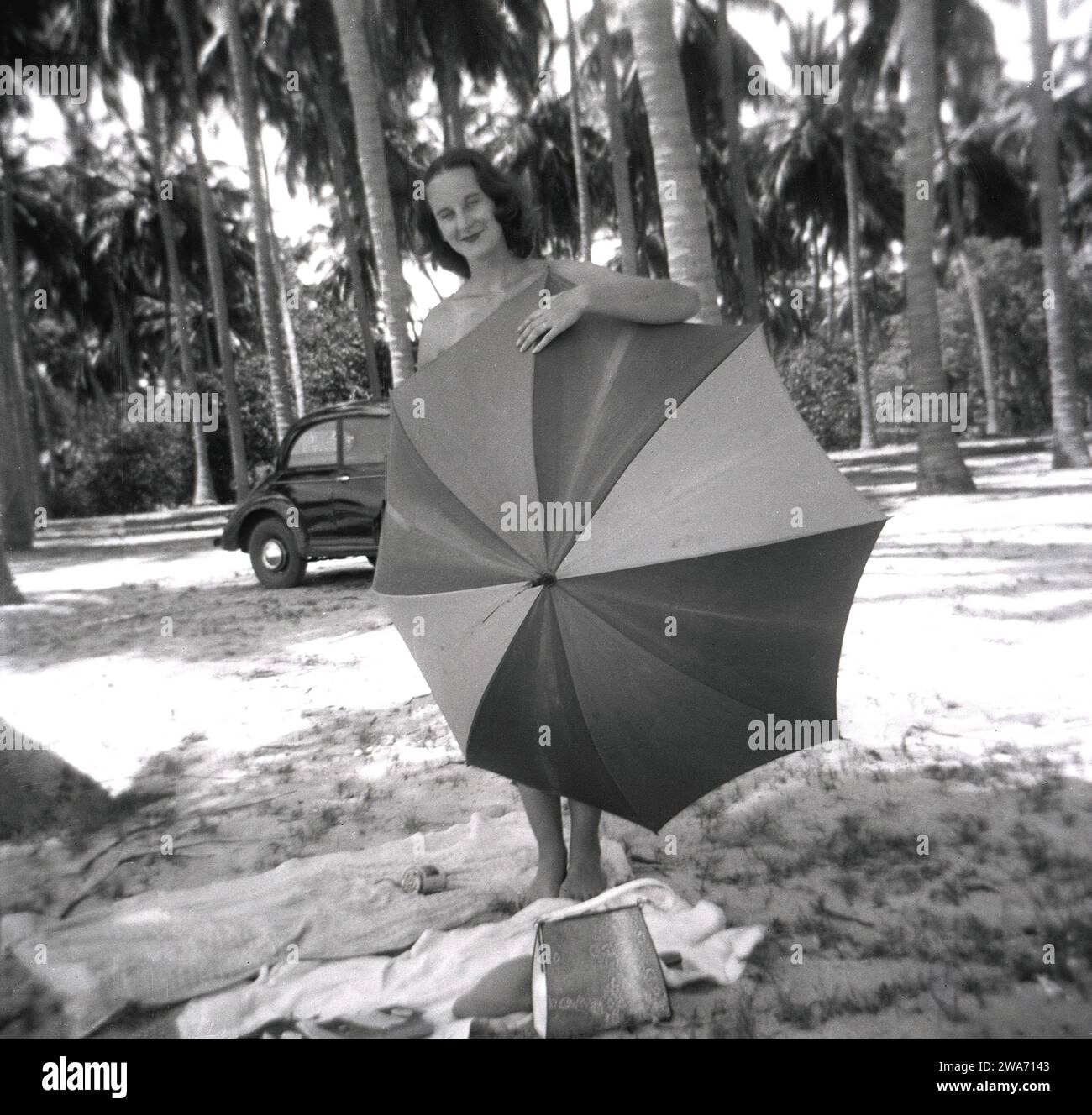 1953, storica, una giovane donna in vacanza sull'isola di Ceylon, in piedi usando un ombrello per nascondere la sua modestia sulla spiaggia. Situata nell'Oceano Indiano nell'Asia meridionale, l'isola divenne una Repubblica Democratica Socialista nel 1972 e cambiò il suo nome in Sri Lanka. Foto Stock