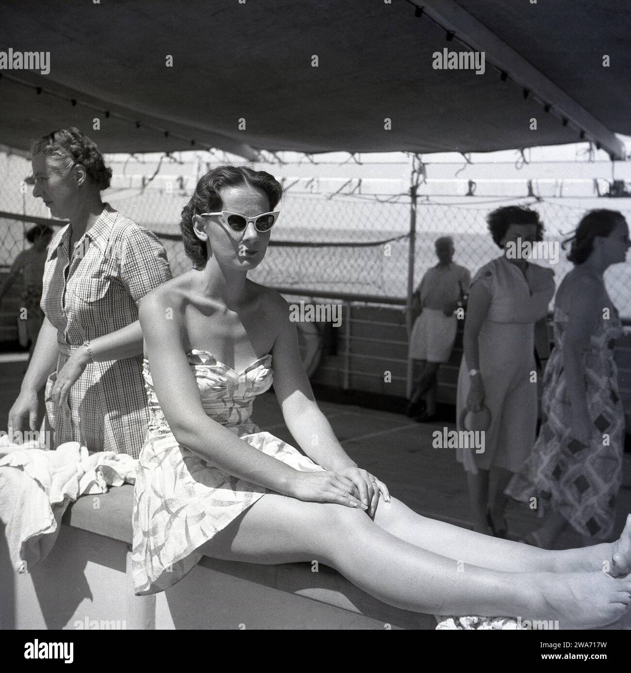 1953, storica, una giovane donna in vacanza sull'isola di Ceylon (Sir Lanka) seduta sul lato di una barca con le gambe e i piedi sulla barriera. Foto Stock