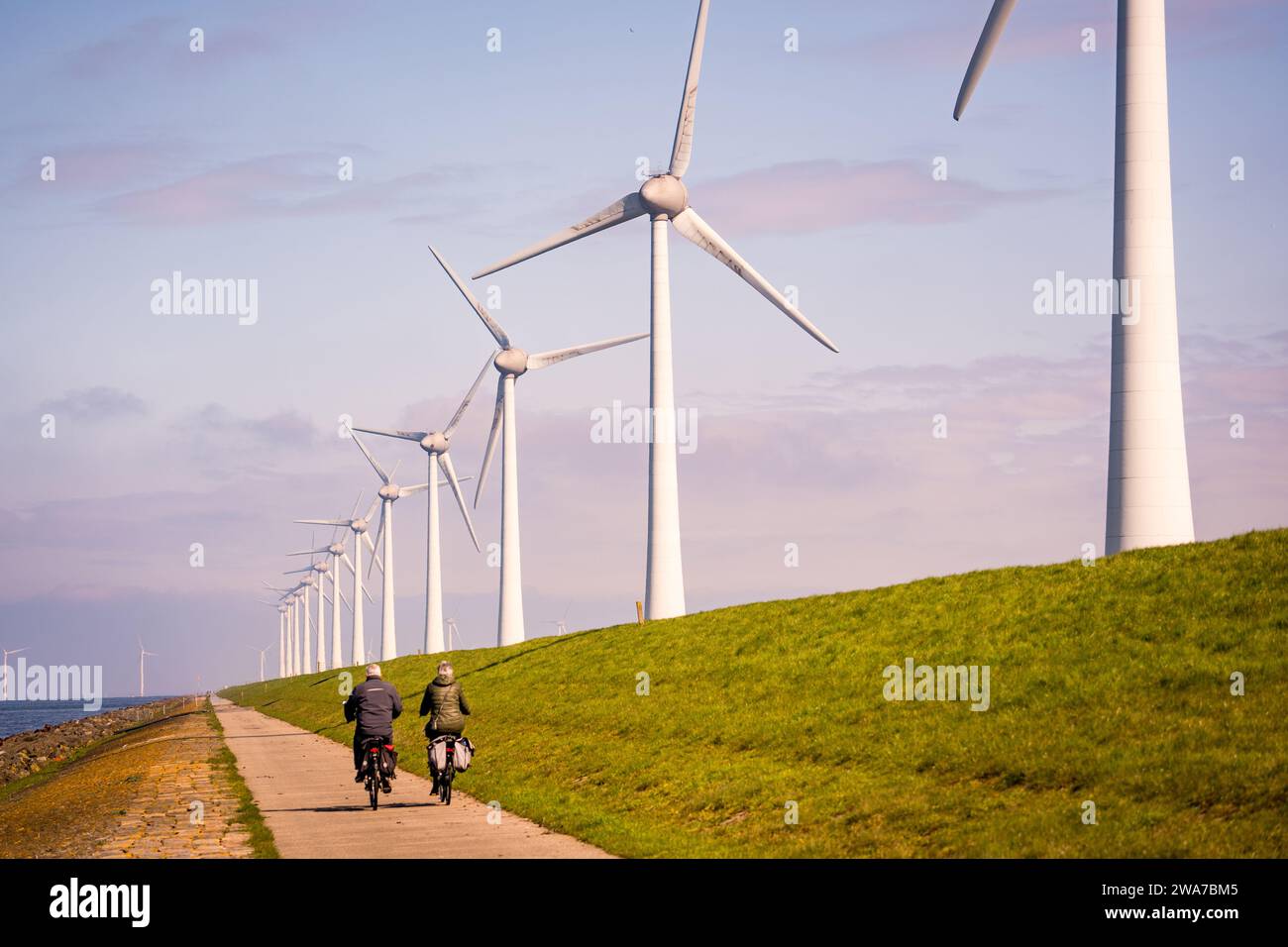 persone che guidano biciclette su strada vicino alle turbine eoliche Foto Stock