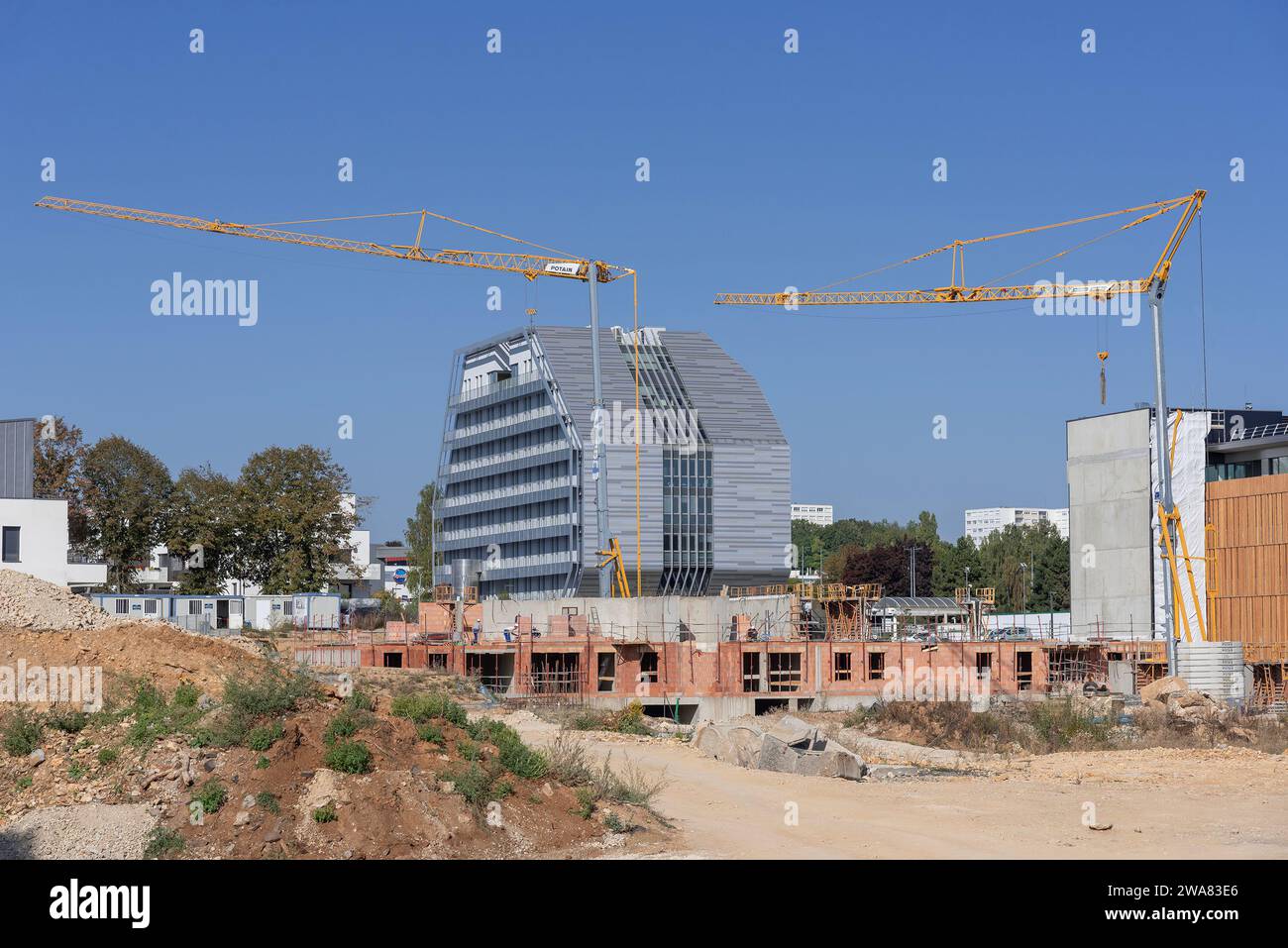 Gru auto-edificanti Potain Hup 40-30 e IGO 50 in un cantiere e un edificio in costruzione con un edificio moderno sullo sfondo. Foto Stock