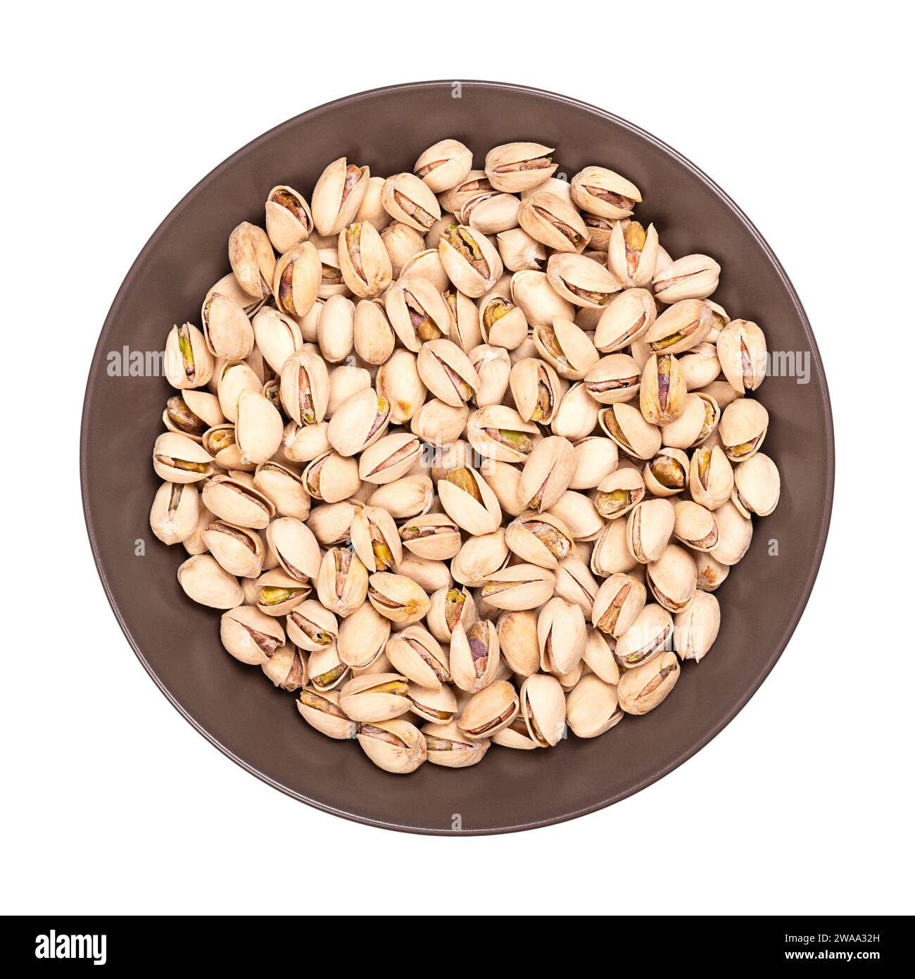 Pistacchi nelle conchiglie, arrostiti e salati, in una ciotola marrone. Croccanti frutti arrostiti di Pistacia vera, con conchiglie aperte e semi all'interno. Foto Stock