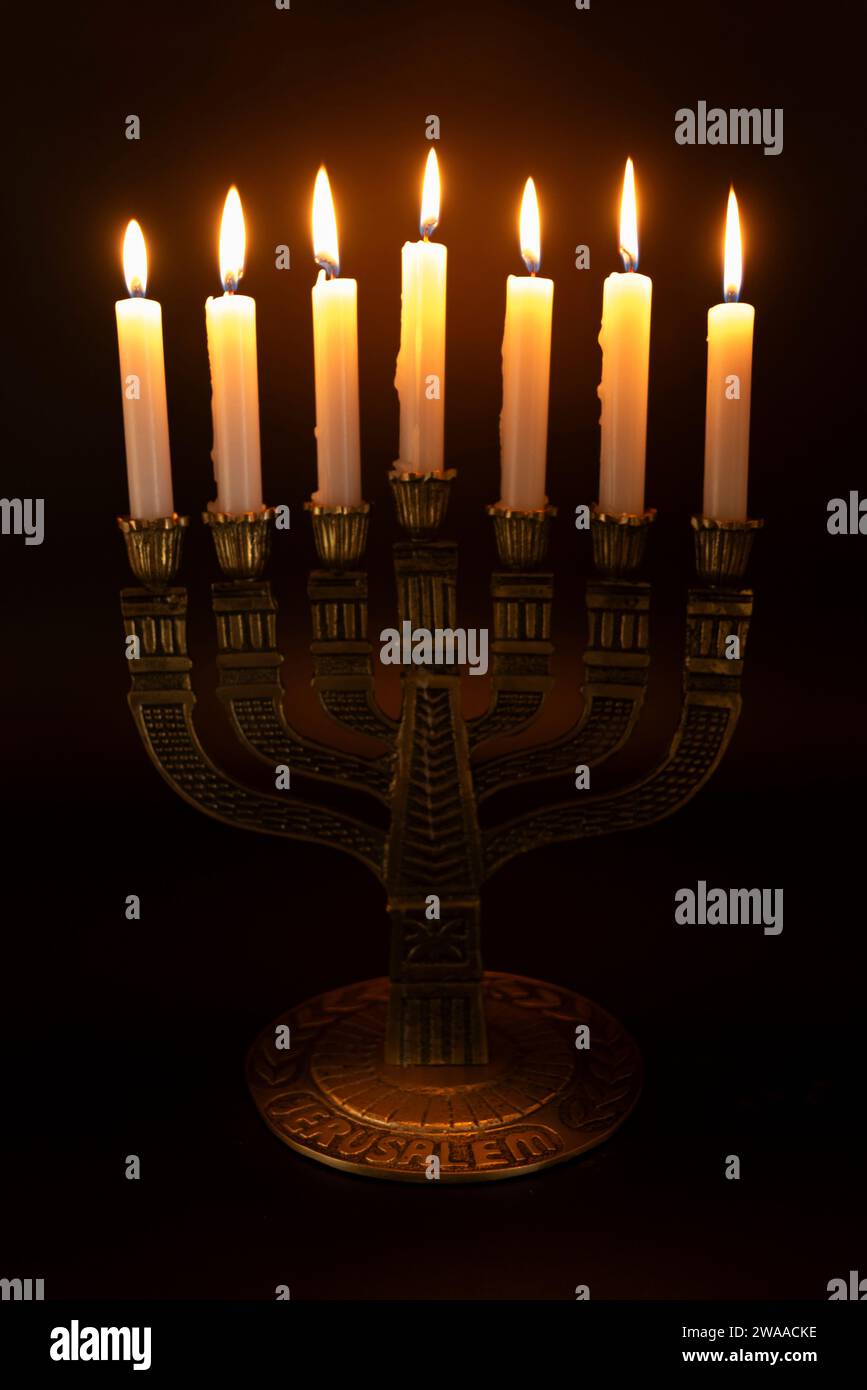 Menorah con la parola GERUSALEMME scritta sulla sua base con 7 candele accese isolate su uno sfondo scuro. Foto Stock