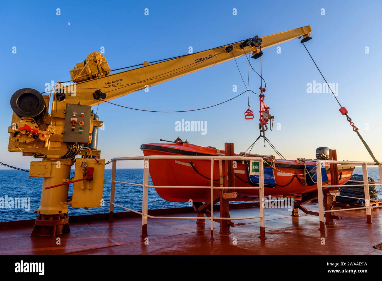 Nave di salvataggio arancione su una grande nave da carico e gru. Trapano uomo a bordo. Addestramento in scialuppa di salvataggio. Foto Stock
