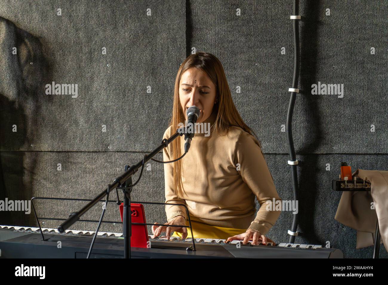 Cantante donna che suona il pianoforte e canta nel microfono, registrando la canzone in uno studio di registrazione audio. Foto Stock