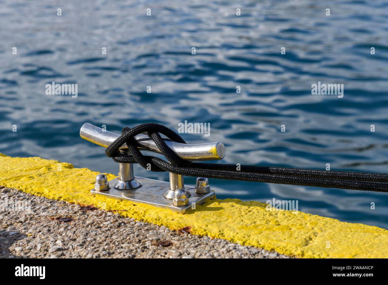 Corda nera per ormeggio con un'estremità annodata legata intorno a un tassello nel porticciolo degli yacht. Attacco tassello. Hardware marino. Concetto di yachting. Foto Stock