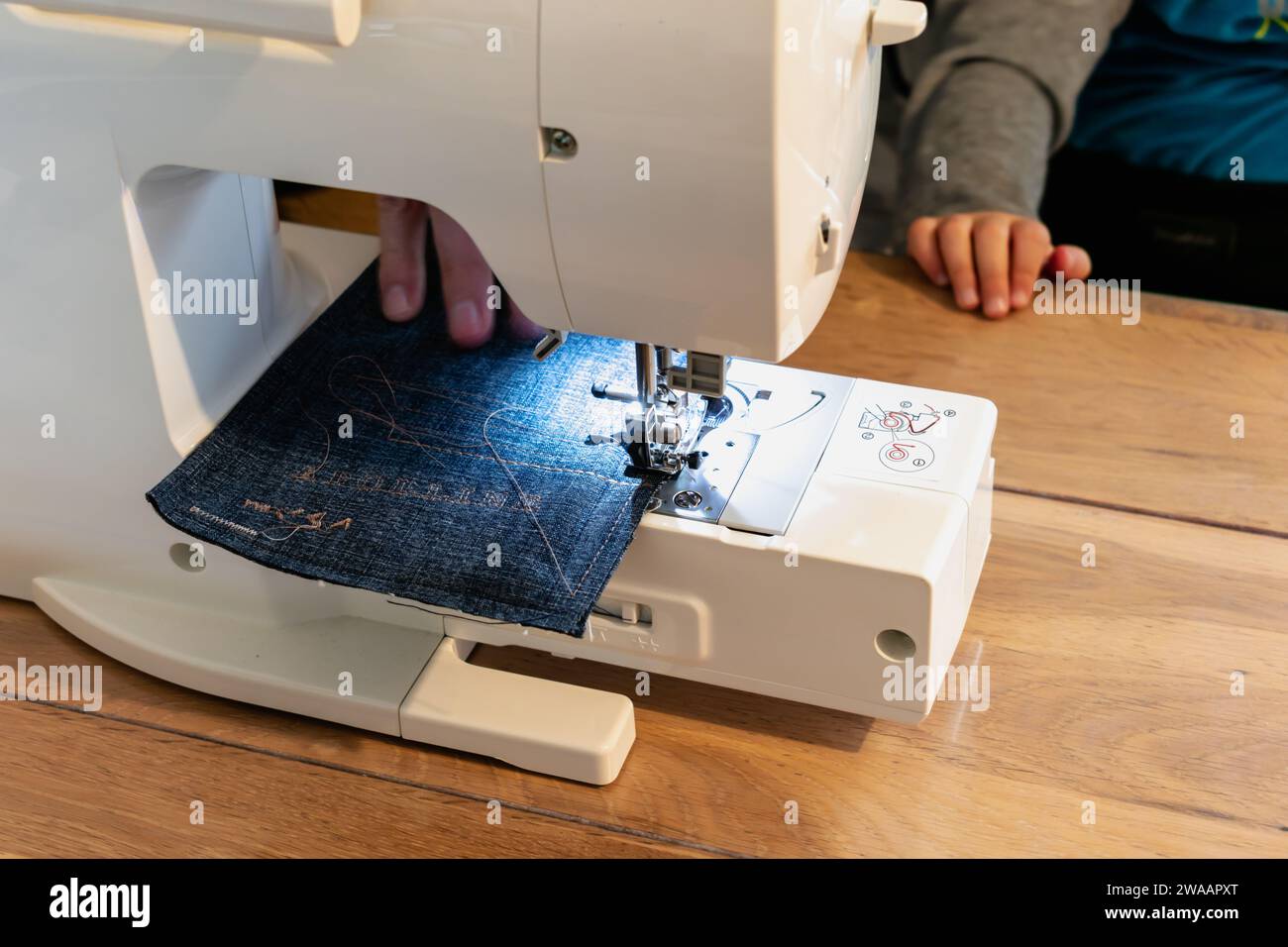 Uomo che usa una macchina da cucire con un indumento blu, per lavori di riparazione, personalizzazione, creazione, upcycling Foto Stock