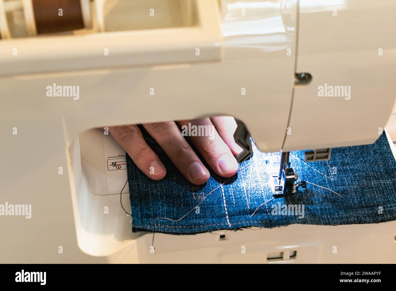 Uomo che usa una macchina da cucire con un indumento blu, per lavori di riparazione, personalizzazione, creazione, upcycling Foto Stock