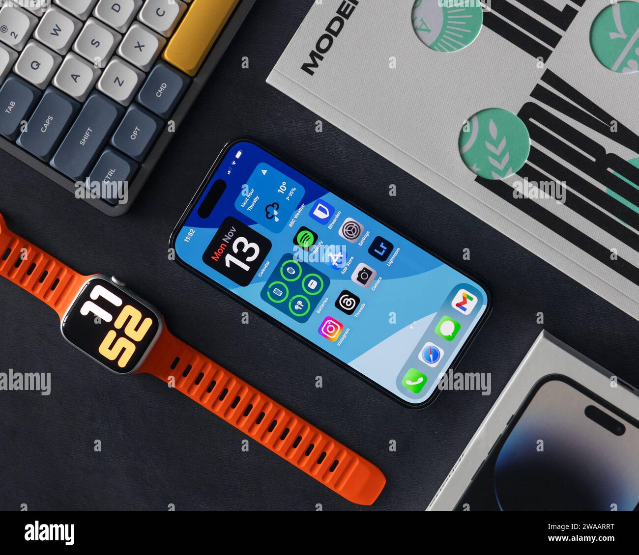 LONDRA - 13 NOVEMBRE 2023: Apple iPhone 14 Pro con sfondo a colori sullo schermo, Apple Watch, vista dall'alto minima EDC con sfondo scuro Foto Stock