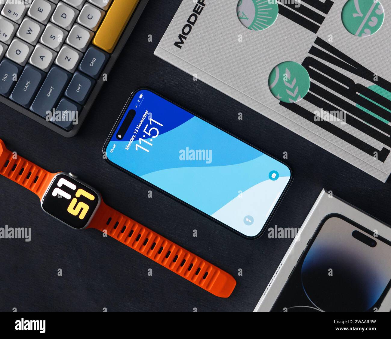 LONDRA - 13 NOVEMBRE 2023: Apple iPhone 14 Pro con sfondo a colori sullo schermo, Apple Watch, vista dall'alto minima EDC con sfondo scuro Foto Stock