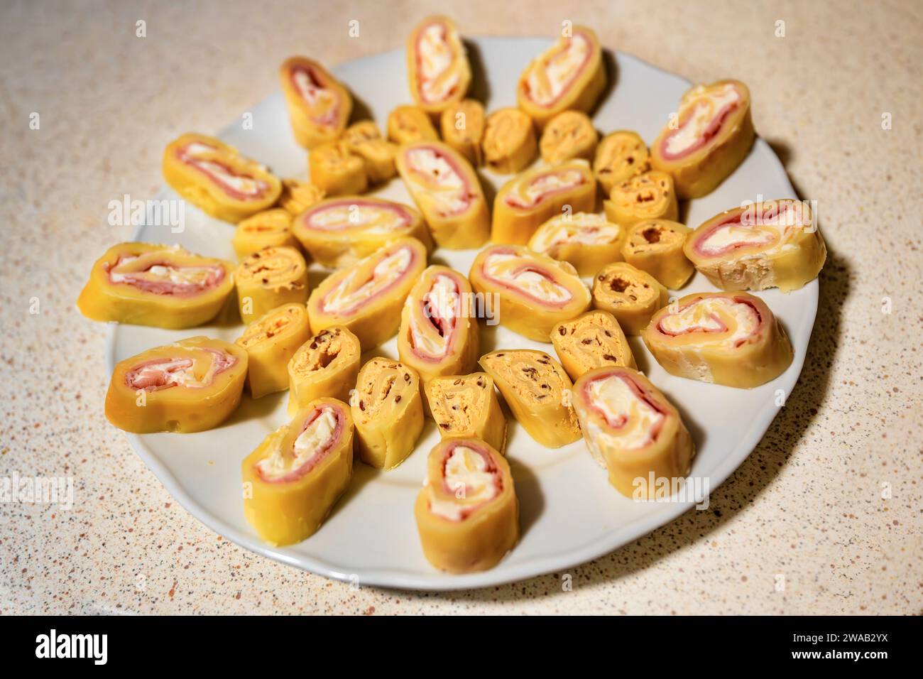 Roulade di formaggio, tagliata su un piccolo pezzo su un piatto bianco, spuntino su un tavolo beige. Ripieno a base di formaggio molle, semi di lino e prosciutto. Foto Stock
