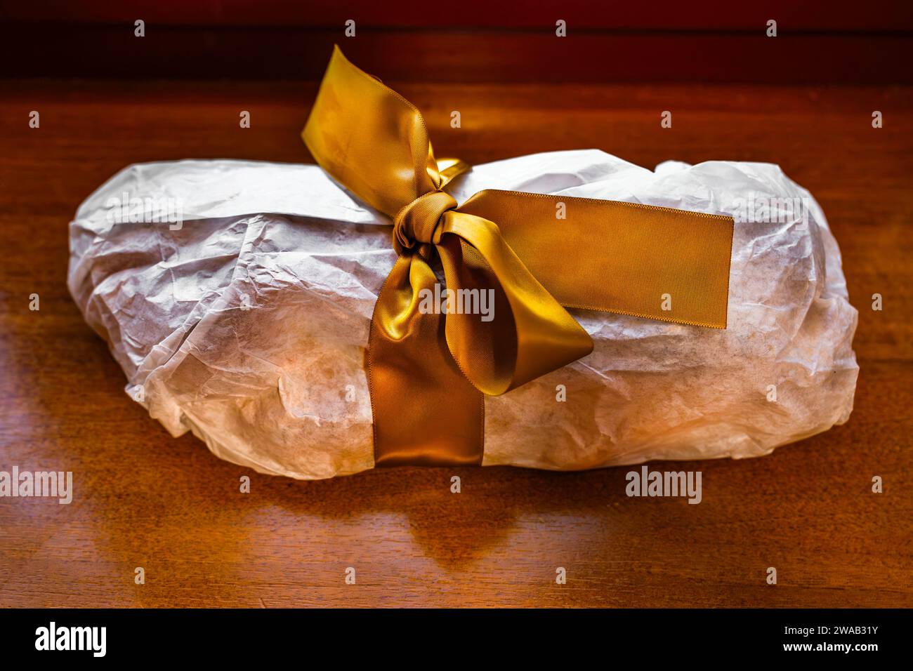Tradizionale pasticceria natalizia avvolta come regalo in carta con nastro dorato su un tavolo di legno. Foto Stock