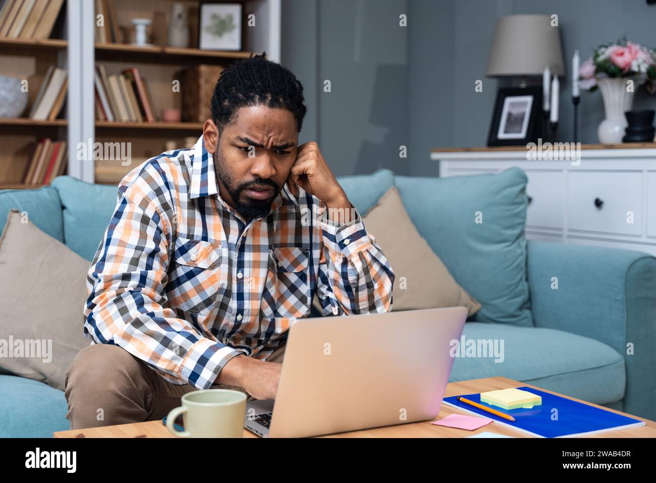 Giovane uomo d'affari freelance o studente di scambio che lavora in remoto dal suo ufficio domestico su un computer portatile, avendo problemi con la connessione Internet o con noi Foto Stock
