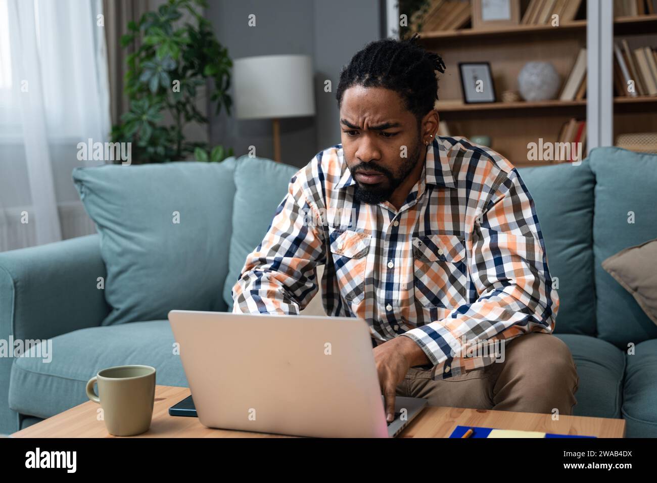 Giovane uomo d'affari freelance o studente di scambio che lavora in remoto dal suo ufficio domestico su un computer portatile, avendo problemi con la connessione Internet o con noi Foto Stock