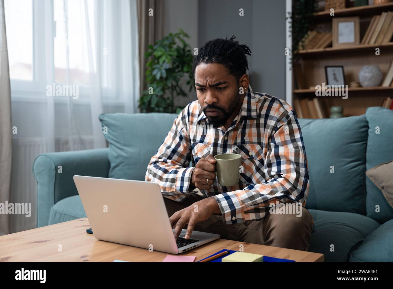 Giovane uomo d'affari freelance o studente di scambio che lavora in remoto dal suo ufficio domestico su un computer portatile, avendo problemi con la connessione Internet o con noi Foto Stock