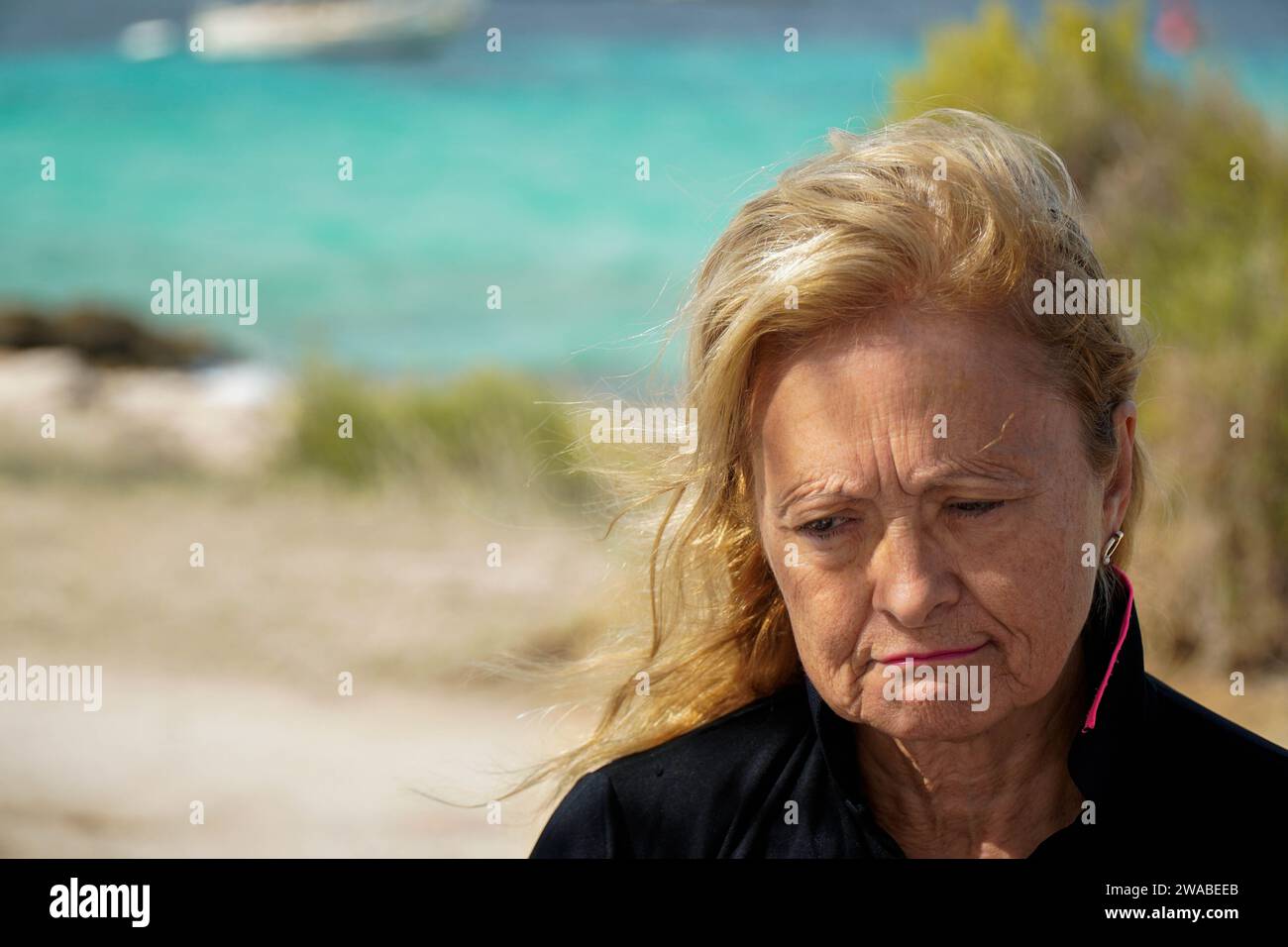 Ritratto ravvicinato di una donna triste e matura in una spiaggia ventosa che guarda in basso Foto Stock
