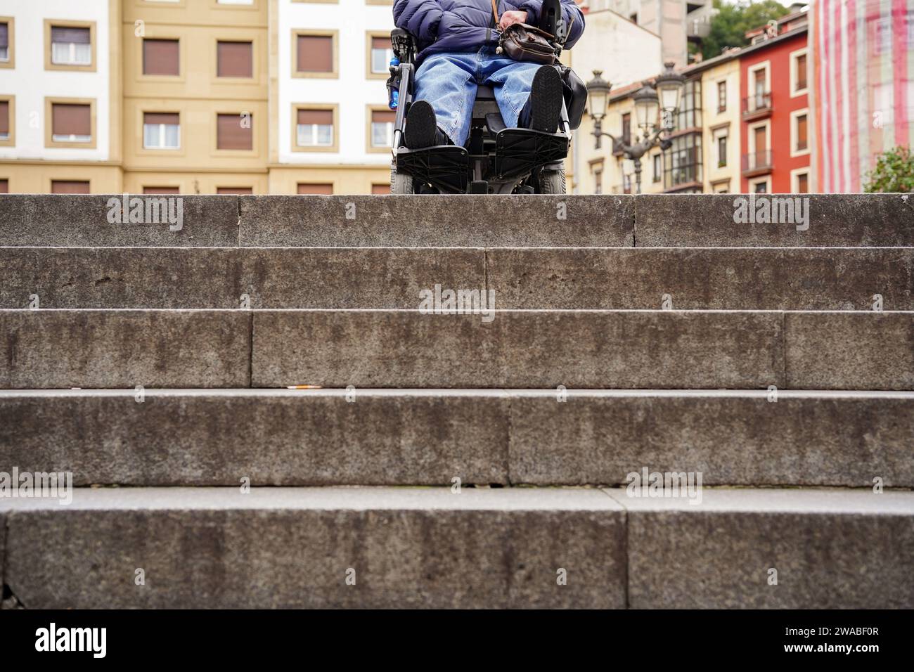 Difficoltà per una persona in sedia a rotelle a scendere le scale urbane Foto Stock