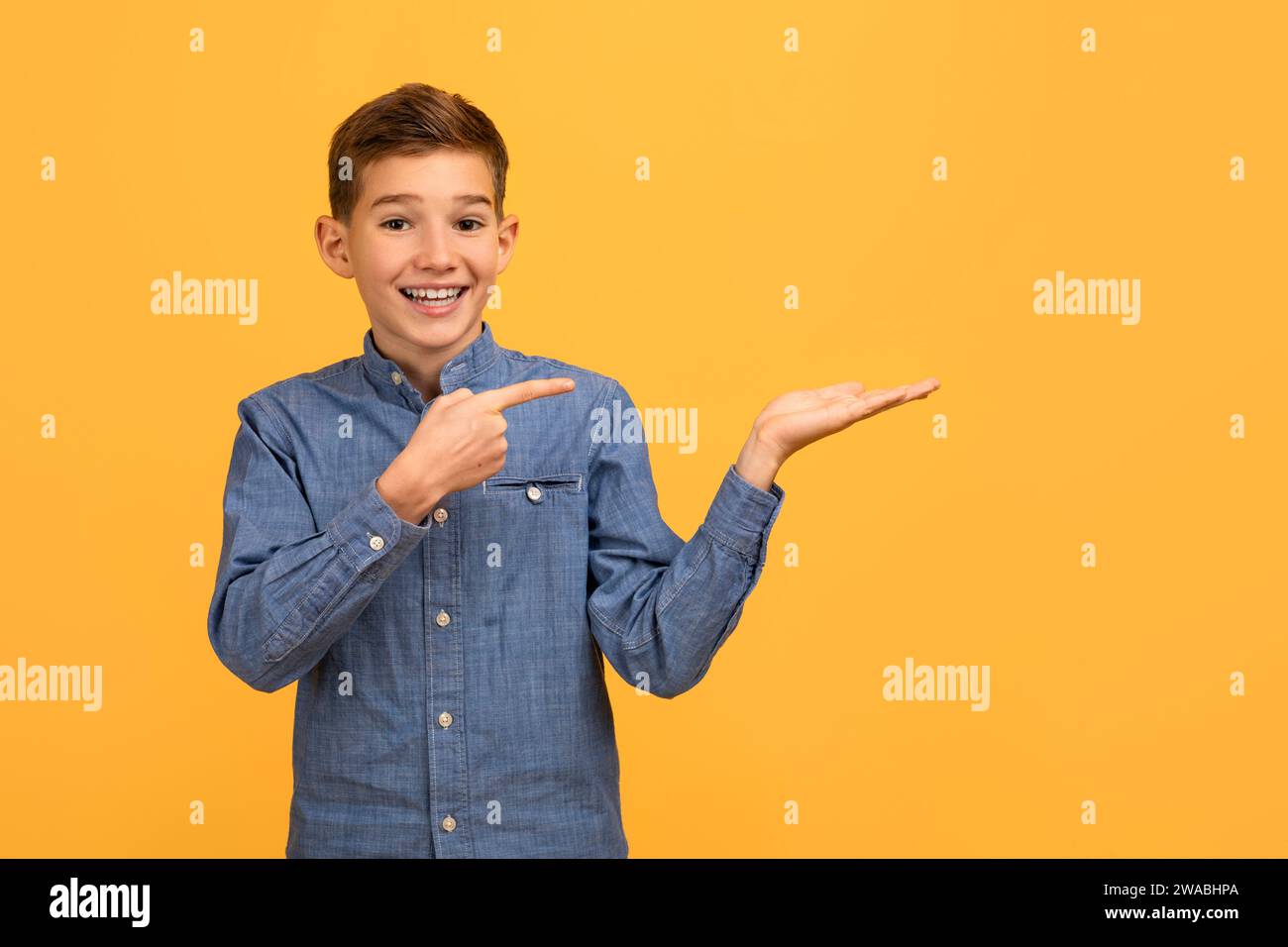 Allegro ragazzo adolescente con camicia in denim che punta sul palmo aperto Foto Stock