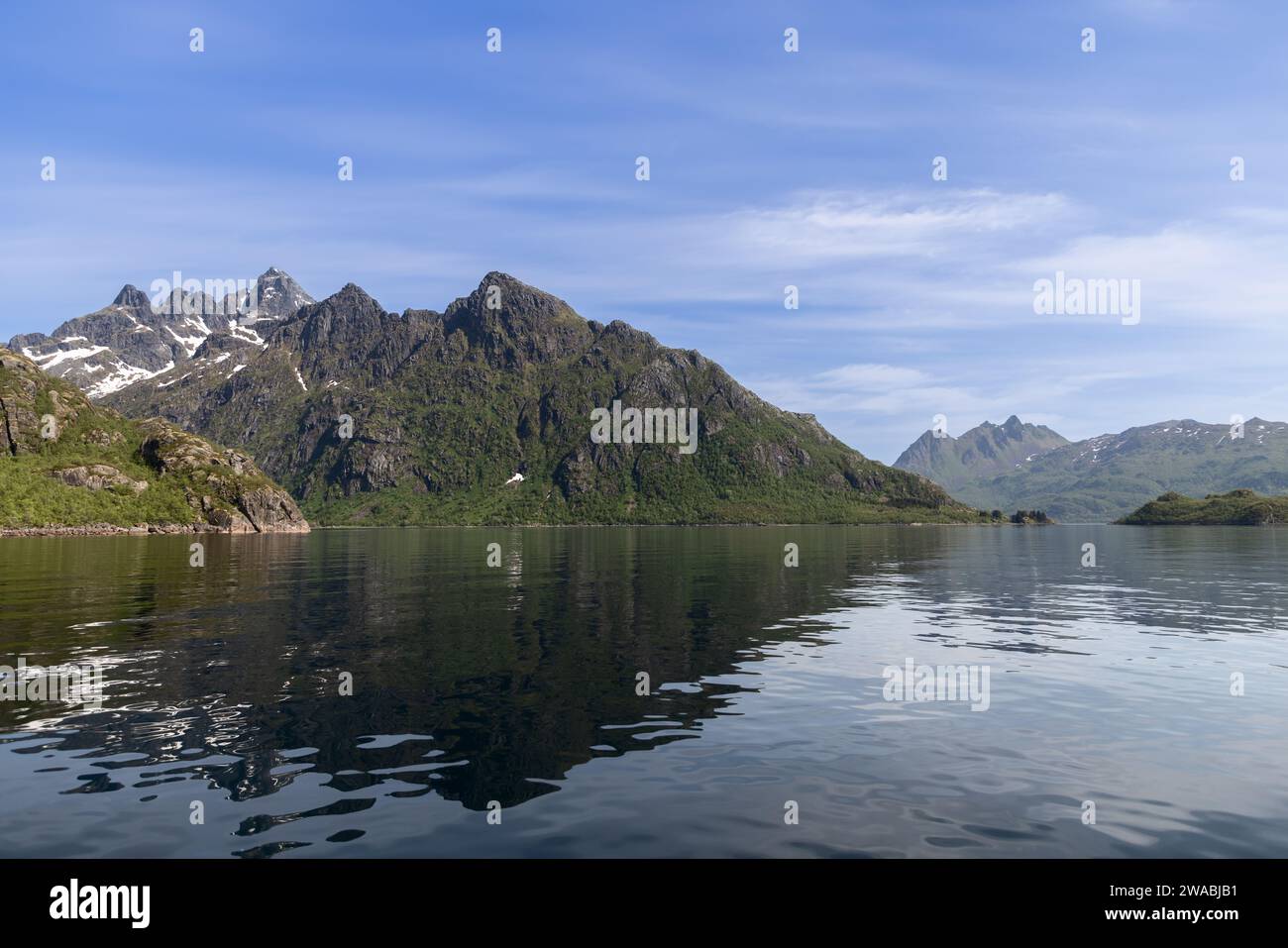 Le tranquille acque di Trollfjorden riflettono la bellezza aspra delle montagne Lofoten, con macchie di neve aggrappate alle loro imponenti altezze Foto Stock