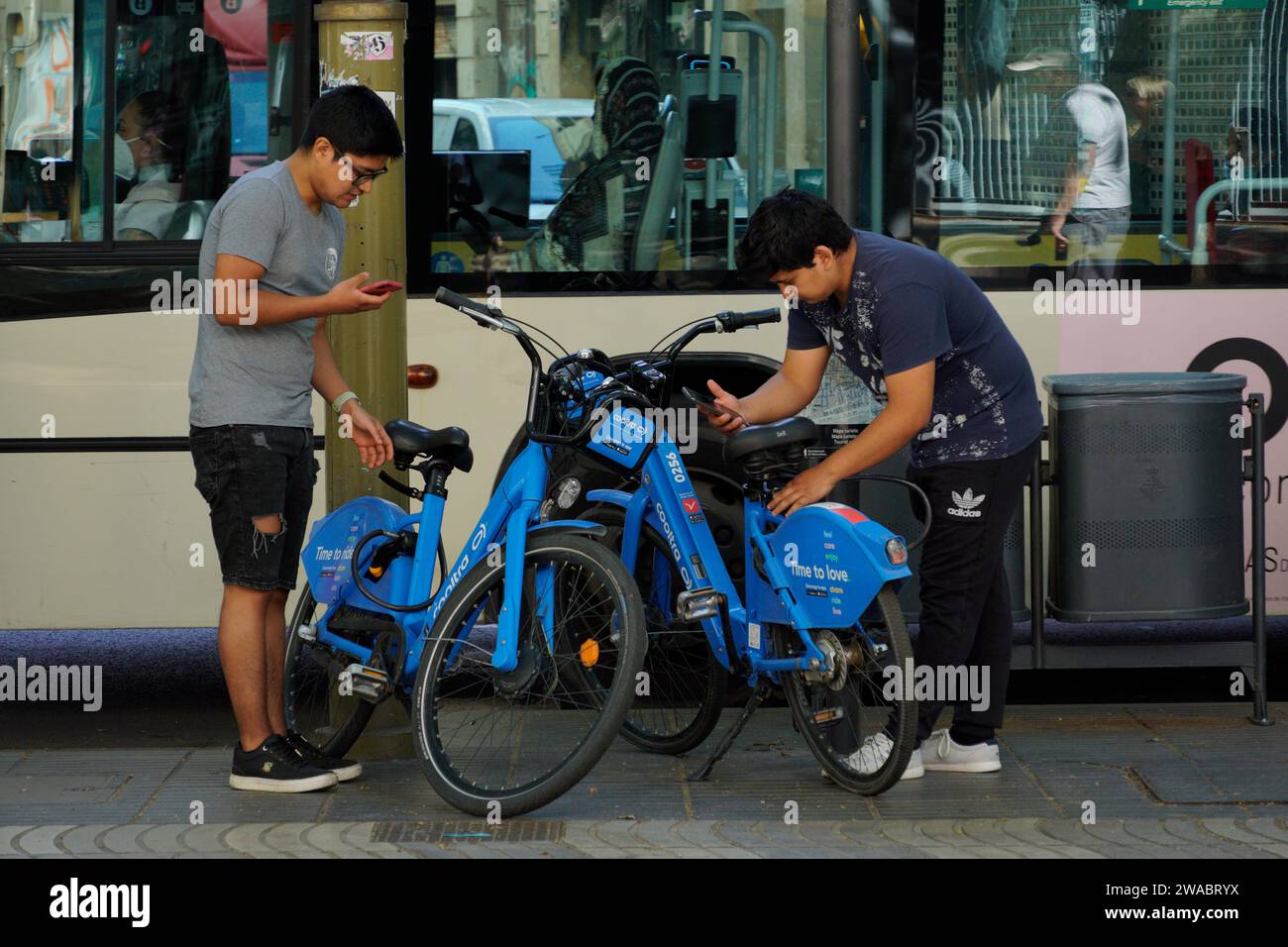 Barcellona, Spagna - 26 maggio 2022: Due adolescenti di origine asiatica stanno per utilizzare il servizio di biciclette elettriche utilizzando l'applicazione per telefono cellulare. Foto Stock