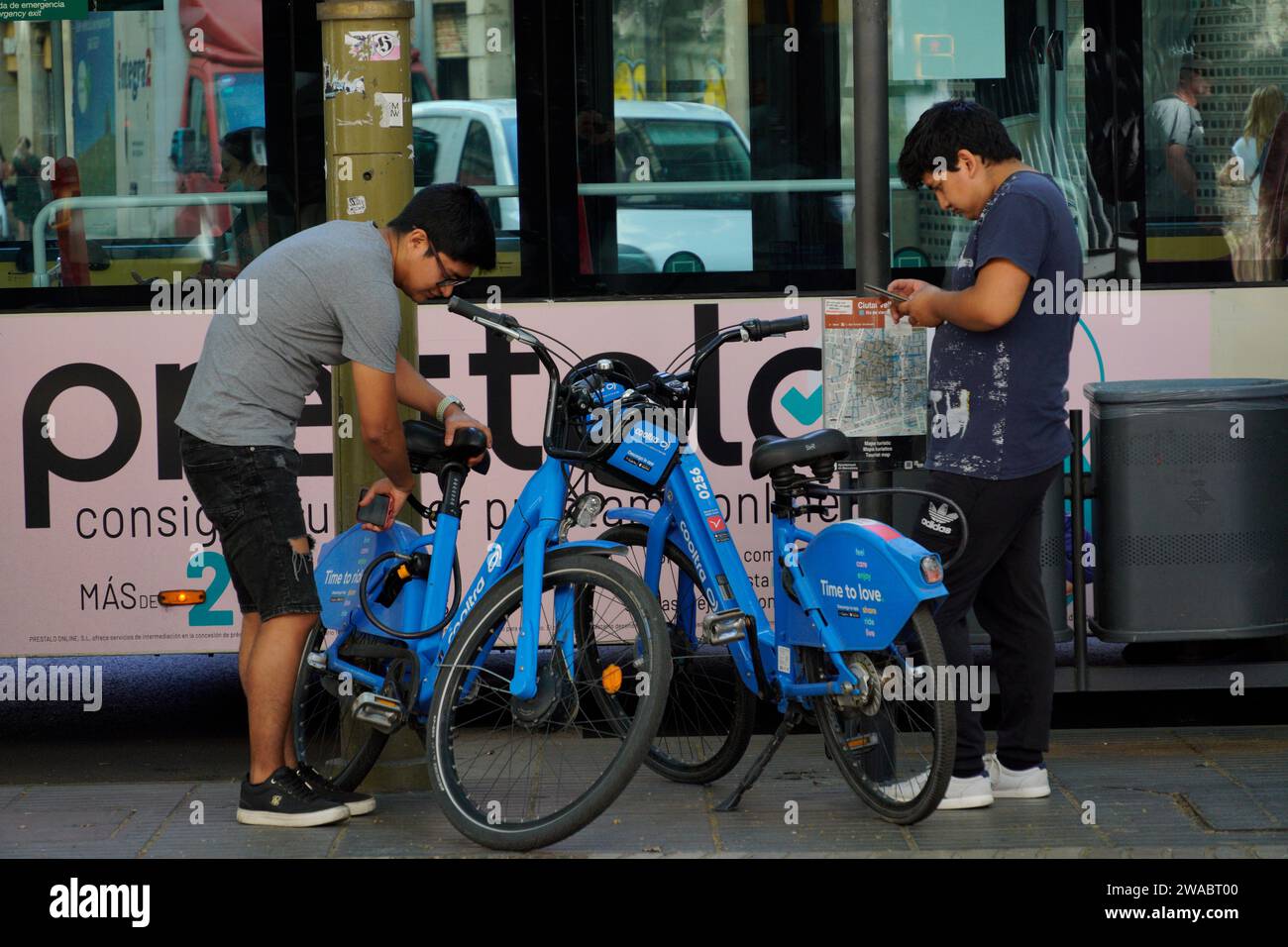 Barcellona, Spagna - 26 maggio 2022: Due adolescenti di origine asiatica stanno per utilizzare il servizio di biciclette elettriche utilizzando l'applicazione per telefono cellulare. Foto Stock