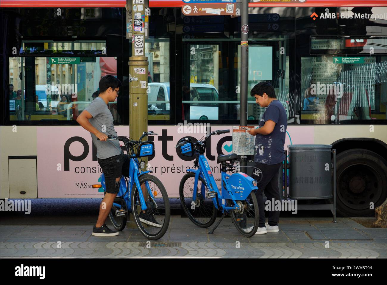 Barcellona, Spagna - 26 maggio 2022: Due adolescenti di origine asiatica stanno per utilizzare il servizio di biciclette elettriche utilizzando l'applicazione per telefono cellulare. Foto Stock