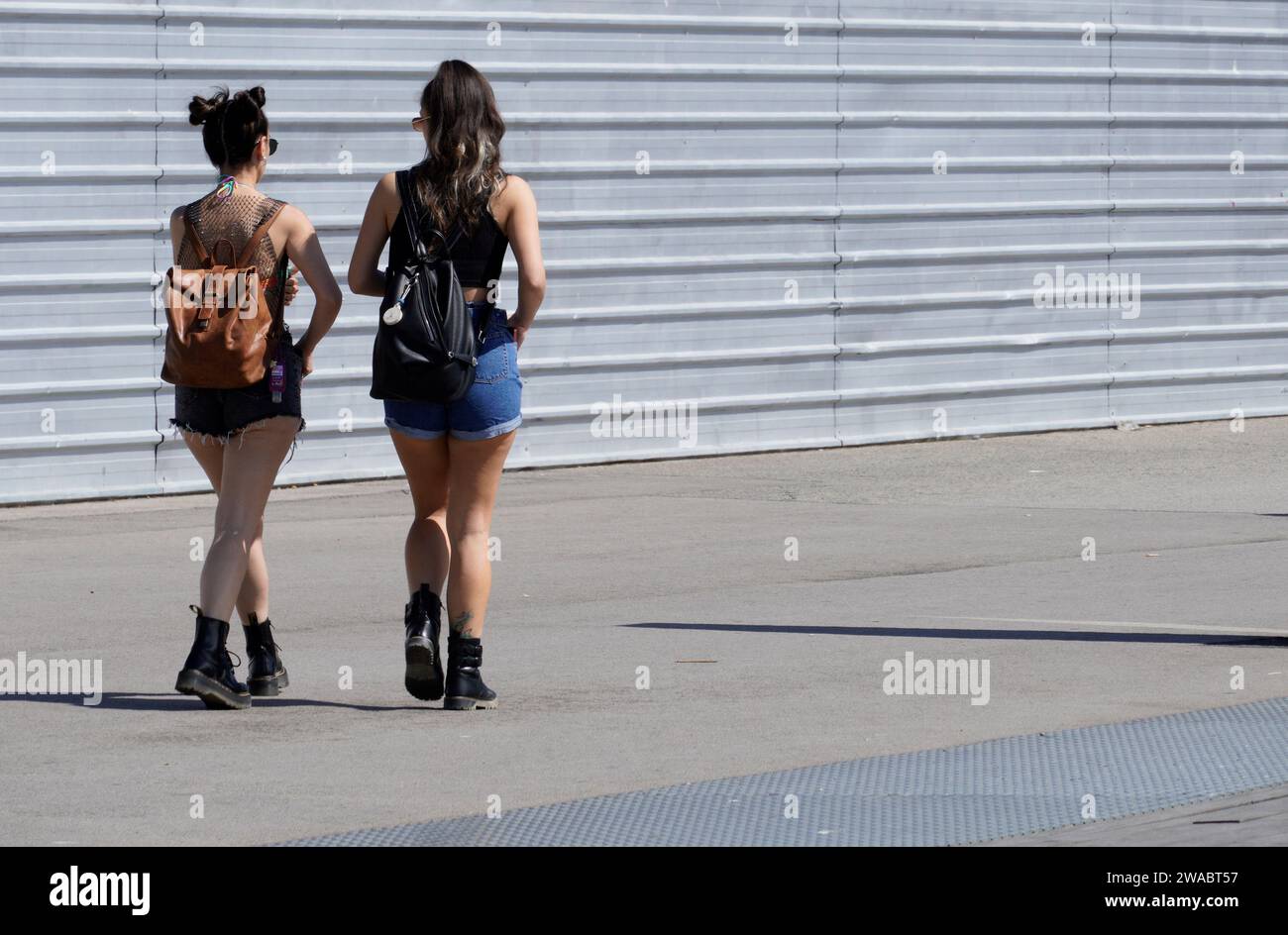 Barcellona, Spagna - 26 maggio 2022: Due ragazze alla moda camminano nella zona di costruzione vestite di pantaloncini jean e stivali militari, entrambe portanti di pantaloncini Foto Stock