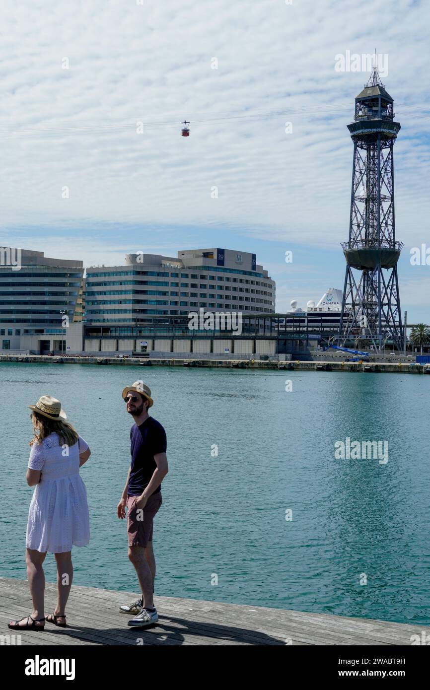 Barcellona, Spagna - 26 maggio 2022: Una coppia visita il porto di Barcellona, con cappelli estivi, una funivia attraversa il cielo delle nuvole bianche. Foto Stock