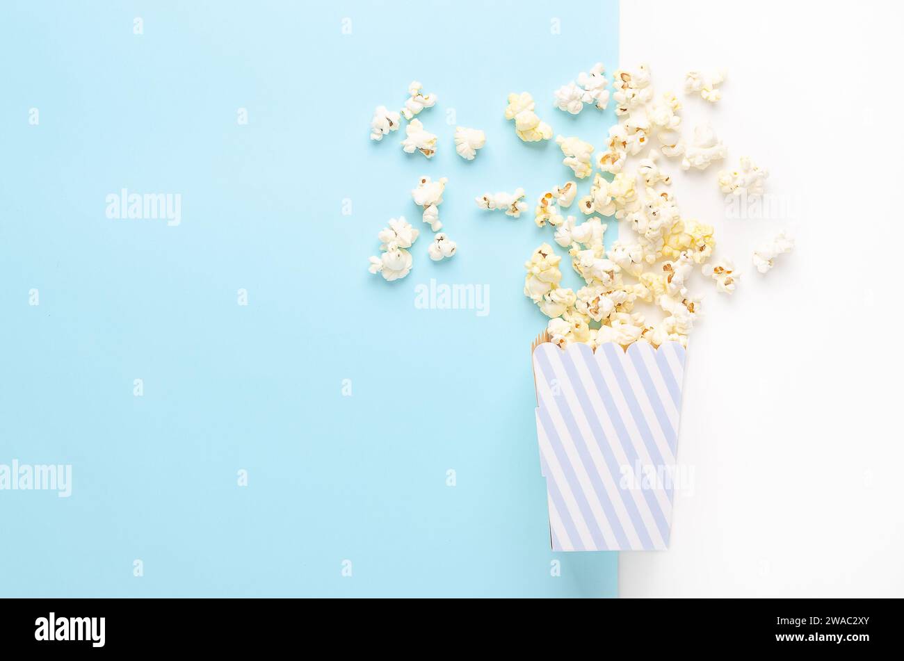 Un secchiello a righe di popcorn su sfondo bianco e azzurro, vista dall'alto e spazio di copia. Foto Stock