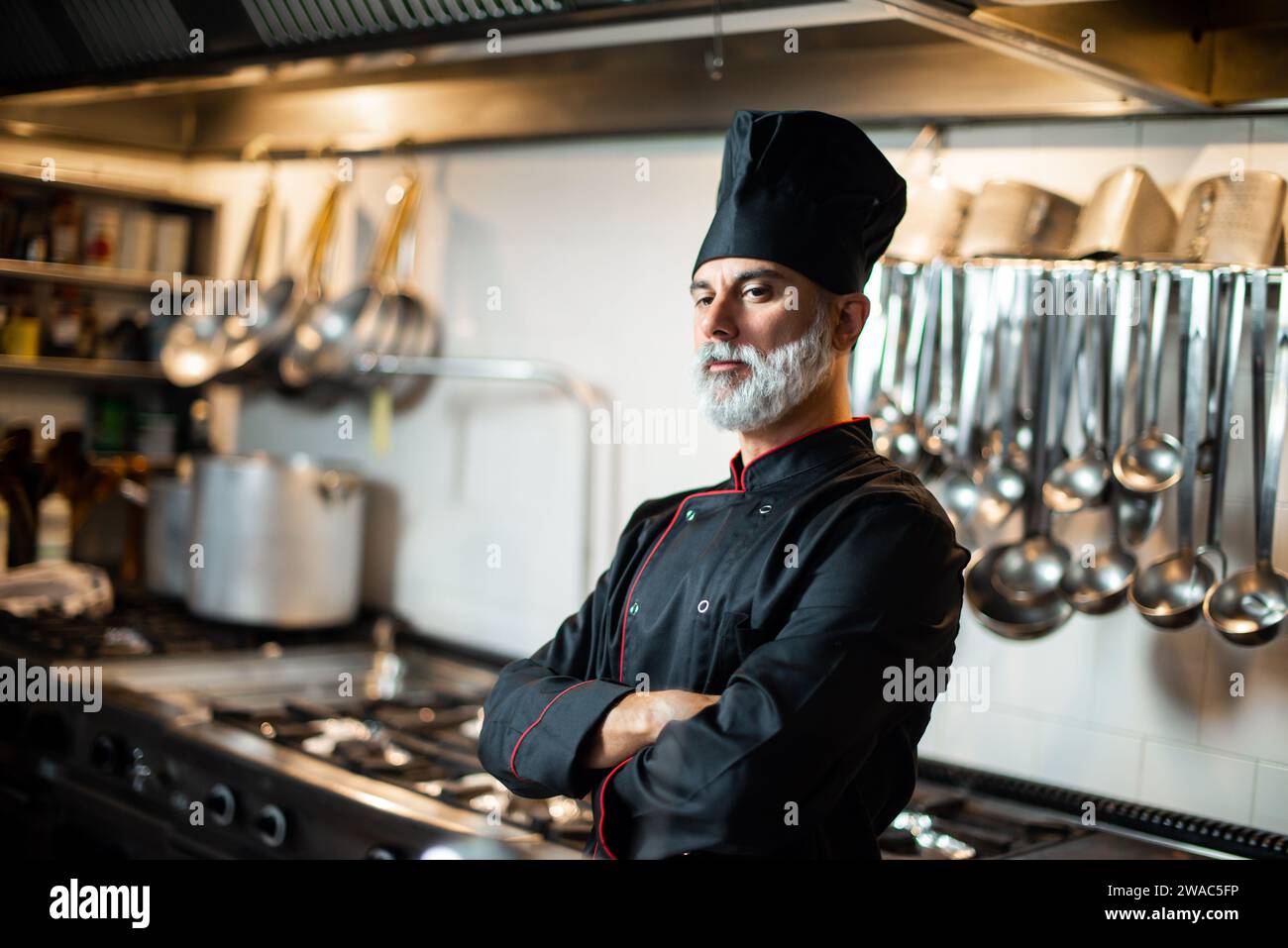 Uno chef maschio maturo e pronto si trova in una cucina commerciale, che mette in mostra le sue competenze culinarie Foto Stock