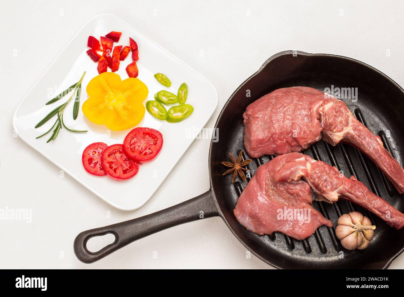 Cuocere la carne con osso, l'aglio e l'anice stellato in padella. Pomodori e peperoni a fette su piatto bianco. Rametto di rosmarino e prezzemolo. Sfondo bianco. Spianatura piatta Foto Stock