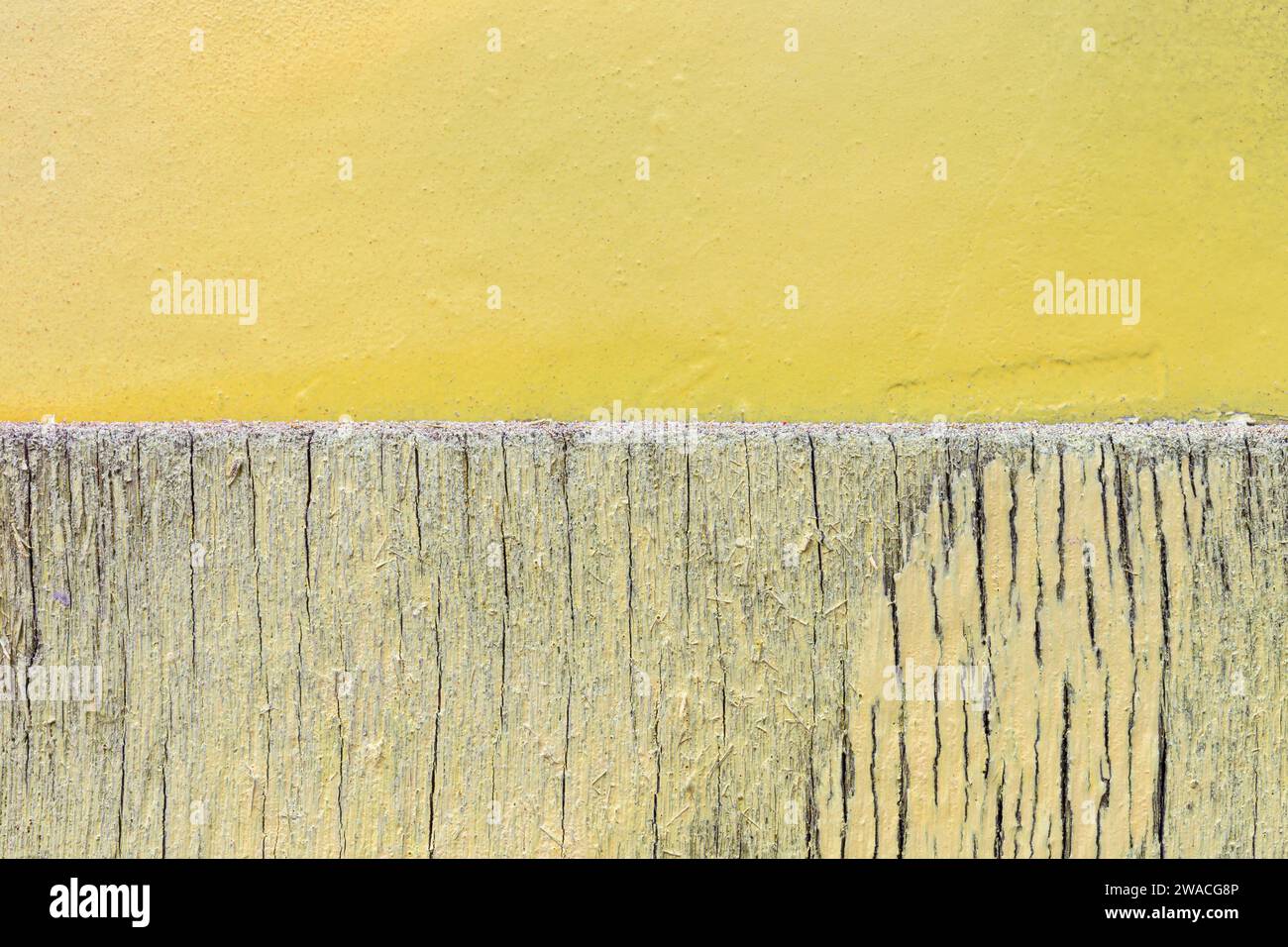 Primo piano di una parete di legno incrinata e intemprata e di una parete di cemento intonacato dipinta di giallo chiaro e luminoso. Sfondo con texture astratta, spazio di copia. Foto Stock