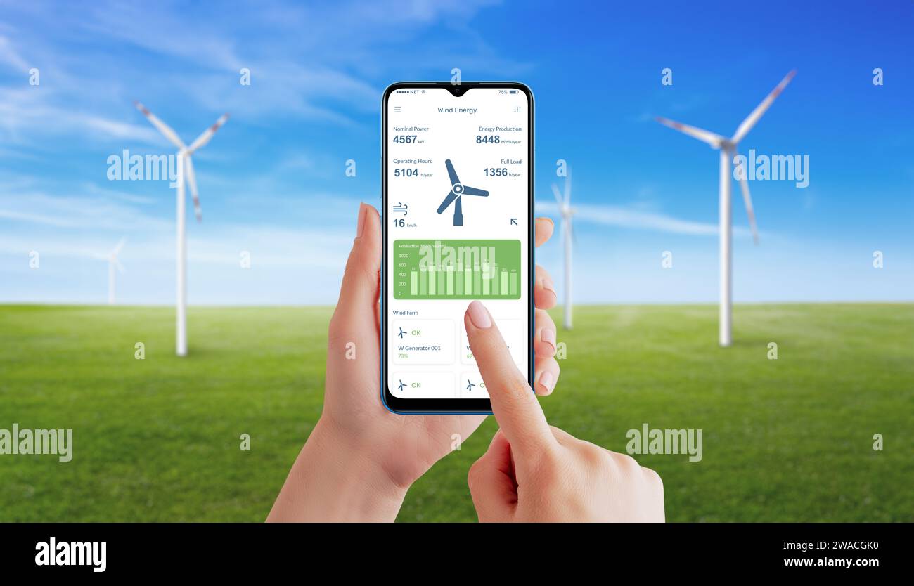 La mano utilizza un'app per generatori eolici per monitorare la produzione di energia. Prato con generatori eolici rotanti sullo sfondo Foto Stock