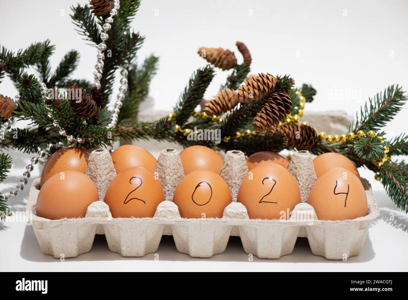 Una scatola di uova con il testo 2024 si trova accanto a un albero di Natale decorato su sfondo bianco, festività e cibo, felice anno nuovo 2024 Foto Stock