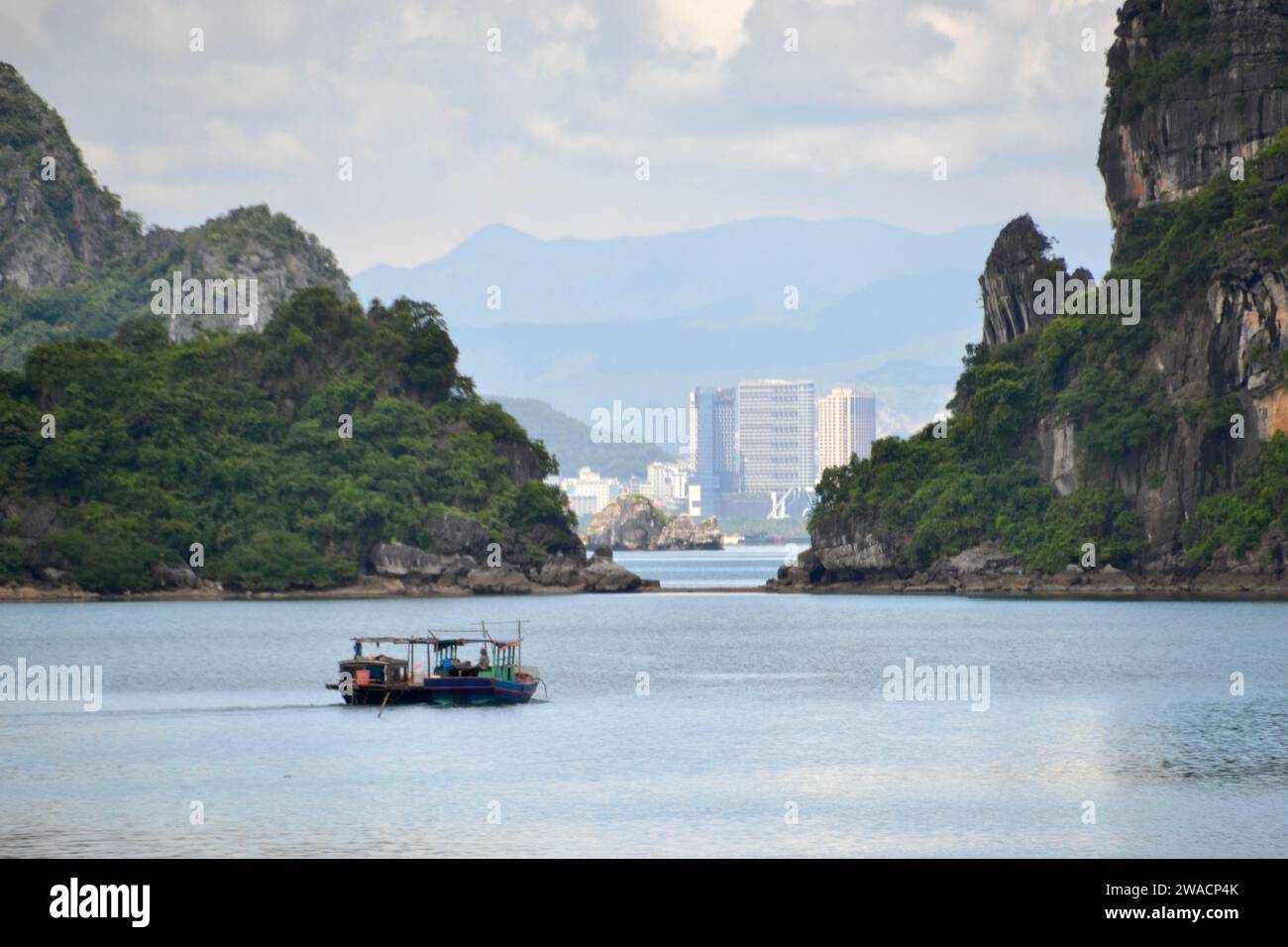 Città portuale vietnamita di ha Long, vista dalla baia di ha Long con grattacieli sullo sfondo e una tradizionale barca spazzatura in primo piano Foto Stock